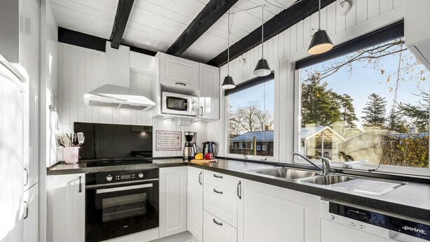 A modern kitchen with white cabinetry, a black stove, a microwave, and a dishwasher. There is a window providing a view of the outside. - "Sampo" - 150m to the fjord by Interhome (Tarm)