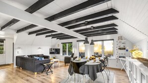 A spacious loft with exposed wooden beams, a dining area with a round table, and a cozy seating area with a sofa and chairs. - "Sampo" - 150m to the fjord by Interhome (Tarm)