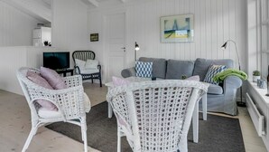 A modern living room with white wicker furniture, a grey sofa, and a television.