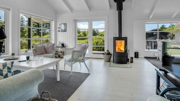 A spacious room with a large window, a white ceiling, and a black wood-burning stove.