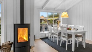 A modern room with a wood-burning stove, white furniture, and a large window offering a view of the outdoors.