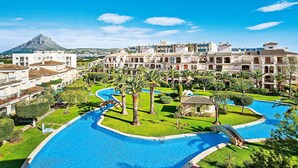 A resort with a large swimming pool, palm trees, and a mountain in the background.