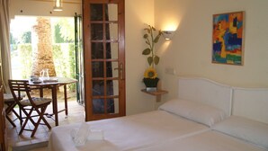 A hotel room with a bed, a table with chairs, a small potted plant, and a painting on the wall.