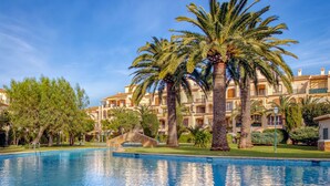 A swimming pool surrounded by palm trees and a building with balconies.