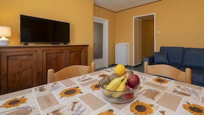 A dining area with a table set for two, a television on a wooden cabinet, and a sofa in the background. - Vacation home Ines by Interhome (San Bernardino)