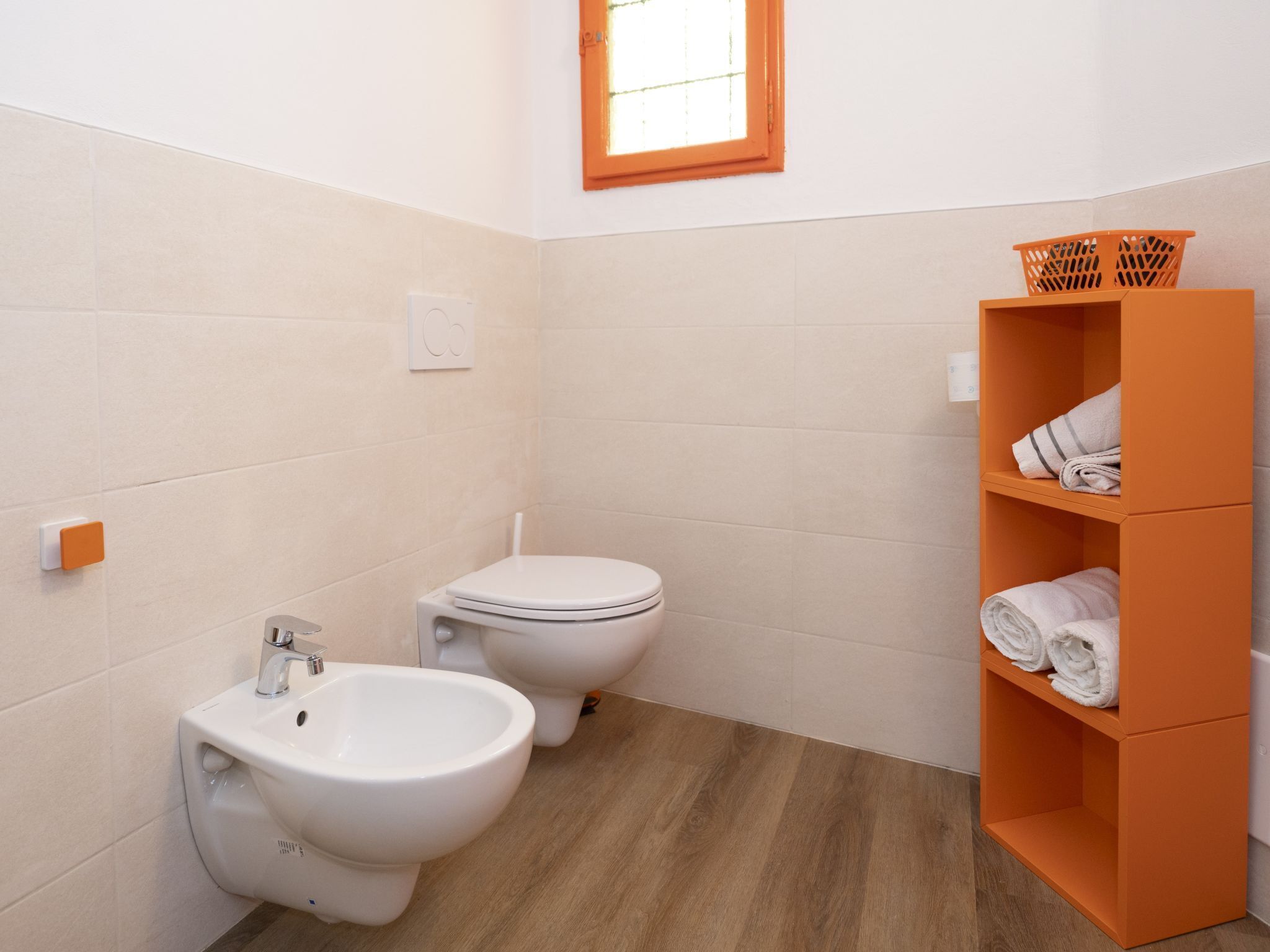 Et lille badeværelse med bidét, toilet og en hylde med håndklæder.