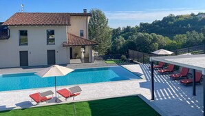 A modern house with a swimming pool, red lounge chairs, and a patio area. - Tenuta Bricco San Giorgio by Interhome (Vinchio)