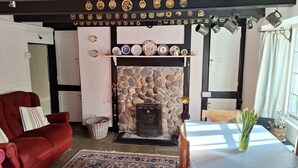 A cozy living room with a stone fireplace, a red sofa, and a dining table with a vase of green plants. - The Old Inn by Interhome (Pentewan)
