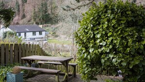 A wooden picnic table with benches, surrounded by a wooden fence and a large bush. - The Old Inn by Interhome (Pentewan)