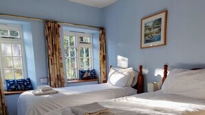 A bedroom with two beds, a hanging light fixture, a window with curtains, and a framed picture on the wall. - The Old Inn by Interhome (Pentewan)