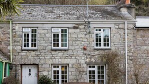 A stone building with a white door, three windows, and a bench outside. - The Old Inn by Interhome (Pentewan)
