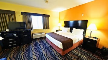 Quarto de hotel com cama, televisão, escrivaninha e mesa de cabeceira.