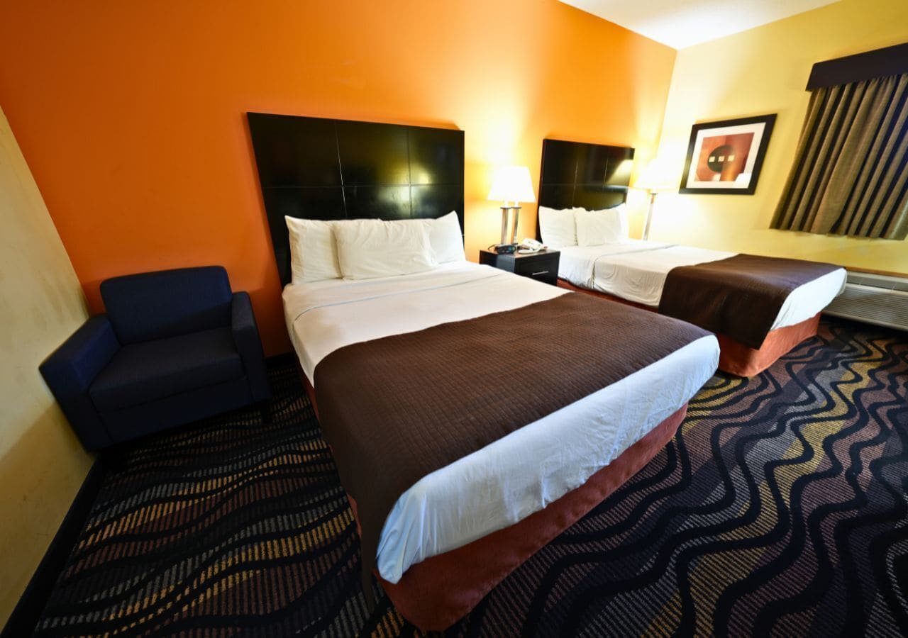 Une chambre d’hôtel avec deux lits, un fauteuil bleu et une moquette à motifs.