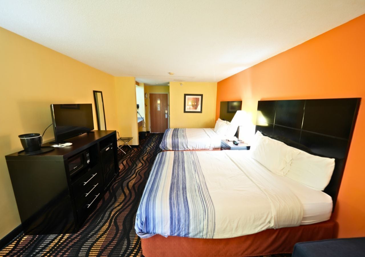 A hotel room with two beds, a desk with a TV, and a dresser.