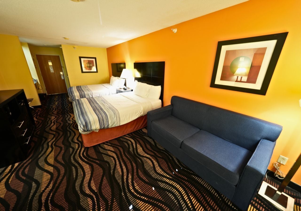 A hotel room with a bed, a blue sofa, a patterned carpet, and a framed picture on the wall.