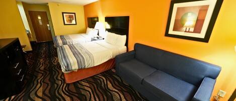 Habitación de hotel con una cama, un sofá azul, alfombra estampada y un cuadro en la pared.