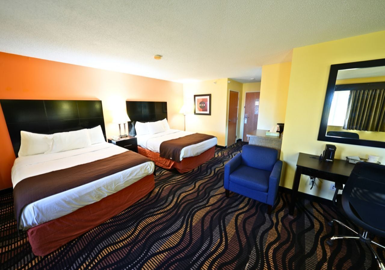 A hotel room with two beds, a desk, a chair, and a mirror.