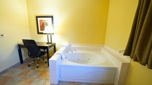 Un baño con una bañera grande, un escritorio con una silla y un cuadro en la pared.