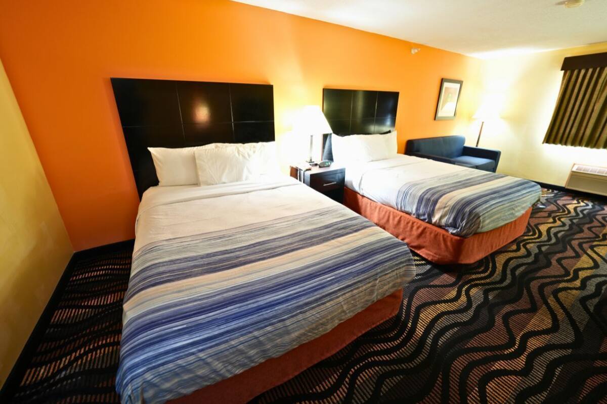 Een hotelkamer met twee bedden, een hoofdbord, een nachtkastje, een lamp en een kamerbreed tapijt met een patroon.