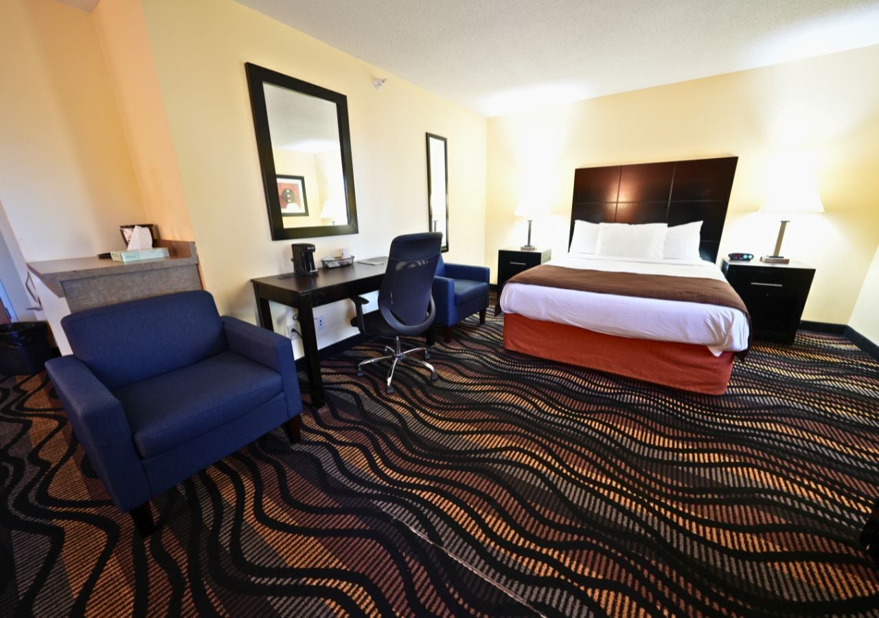 Una habitación de hotel con una cama, un escritorio, una silla y un espejo grande.