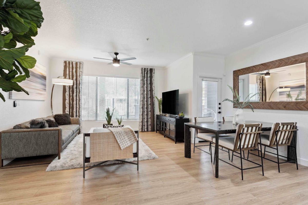 A modern living room with a sofa, a dining table with chairs, a TV, and a large mirror.