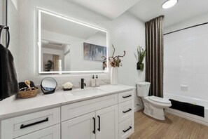 A modern bathroom with a white vanity, a large mirror, a toilet, and a shower area. - The Laurel Apartments in Chandler (Chandler)