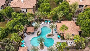 Ein Luftbild eines Resorts mit einem zentral gelegenen Swimmingpool, umgeben von Palmen und Liegebereichen.