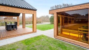 Une structure moderne en bois, dotée d’un patio couvert et d’une pièce fermée par des baies vitrées.