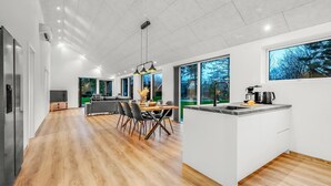 Une cuisine moderne dotée d’un îlot central, de grandes fenêtres et d’un coin repas avec une table et des chaises en bois.