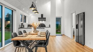 Une cuisine moderne avec un coin repas, comprenant une table en bois, des chaises noires et des luminaires suspendus.