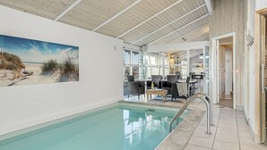 Ein Swimmingpool mit Blick auf den Strand, ein Essbereich mit Stühlen und Tischen sowie eine durchgehende Tür sichtbare Küche.
