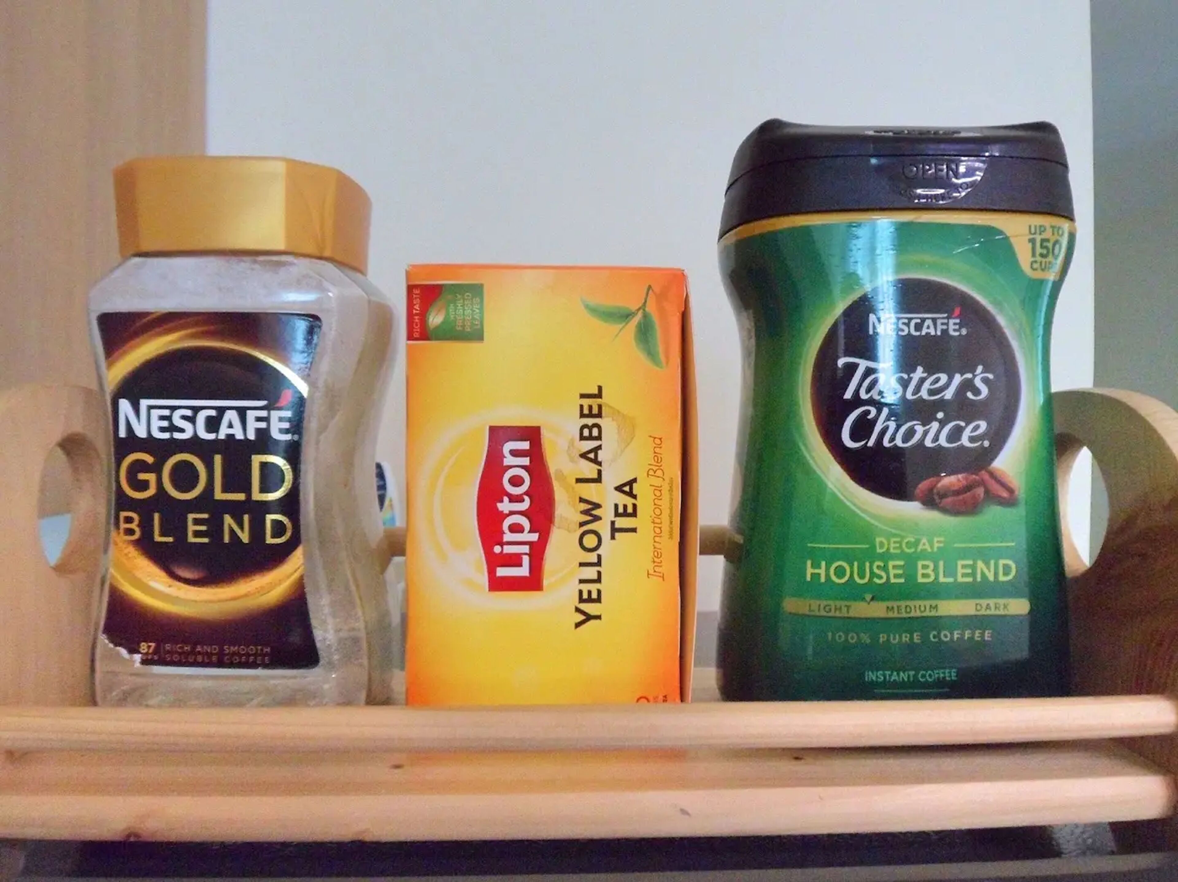 Une étagère présentant trois produits à base de café : Nescafe Gold Blend, thé Lipton Yellow Label et Nescafe Taster’s Choice, variété décaféinée.
