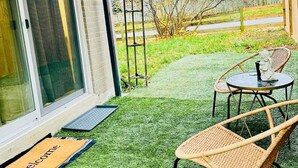A covered patio with artificial grass, a wicker chair, a small table, and a welcome mat. - Pet friendly private backyard Garden studio (Pickering)