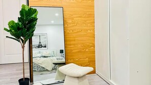 A modern room with a wooden accent wall, a large mirror, a potted plant, a white sofa, and a white cabinet. - Pet friendly private backyard Garden studio (Pickering)