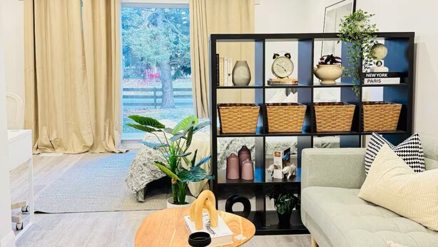 A modern living room with a sofa, a coffee table, a bookshelf, and a view of the outdoors. - Pet friendly private backyard Garden studio (Pickering)