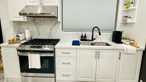 A modern kitchen with white cabinets, a stainless steel stove, and a black backsplash. - Pet friendly private backyard Garden studio (Pickering)