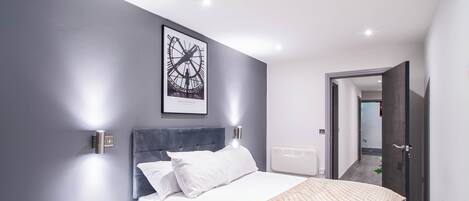 A modern bedroom with a bed, bedside table, and a framed picture on the wall.