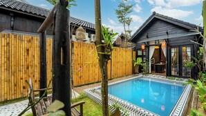 Un patio trasero con piscina, valla de madera y un edificio de arquitectura tradicional.