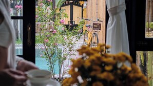 Vista a través de una puerta que muestra una mesa, un jarrón con flores y una bicicleta al fondo.