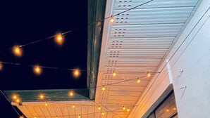A covered outdoor area with string lights, a potted plant, and a table with chairs.
