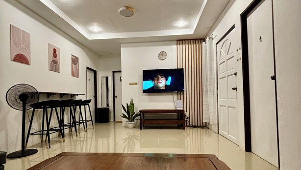 A modern living room with a wooden coffee table, a flat-screen TV mounted on the wall, a ceiling fan, and a potted plant.