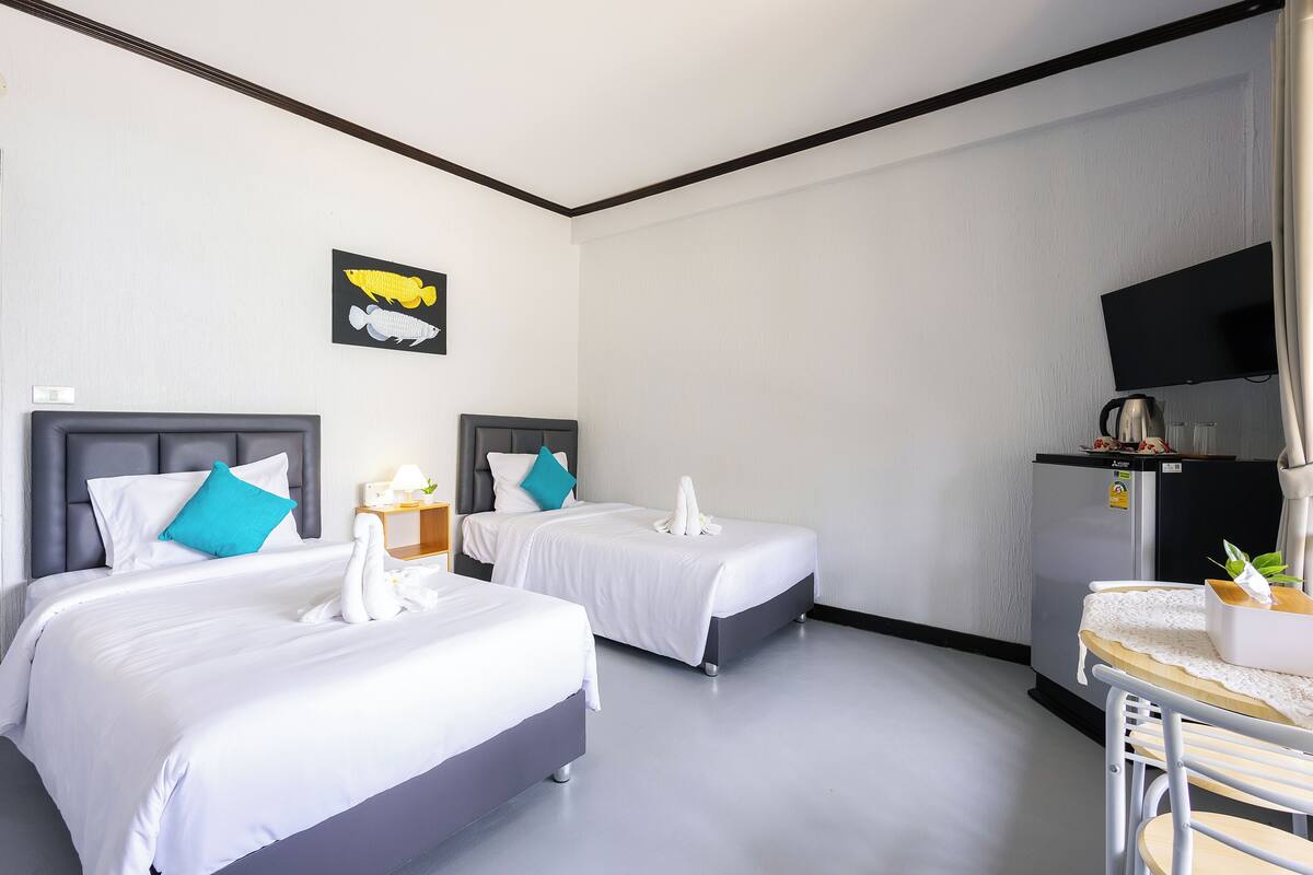 A hotel room with two beds, a flat-screen TV, a minibar, and a small table with a plant.