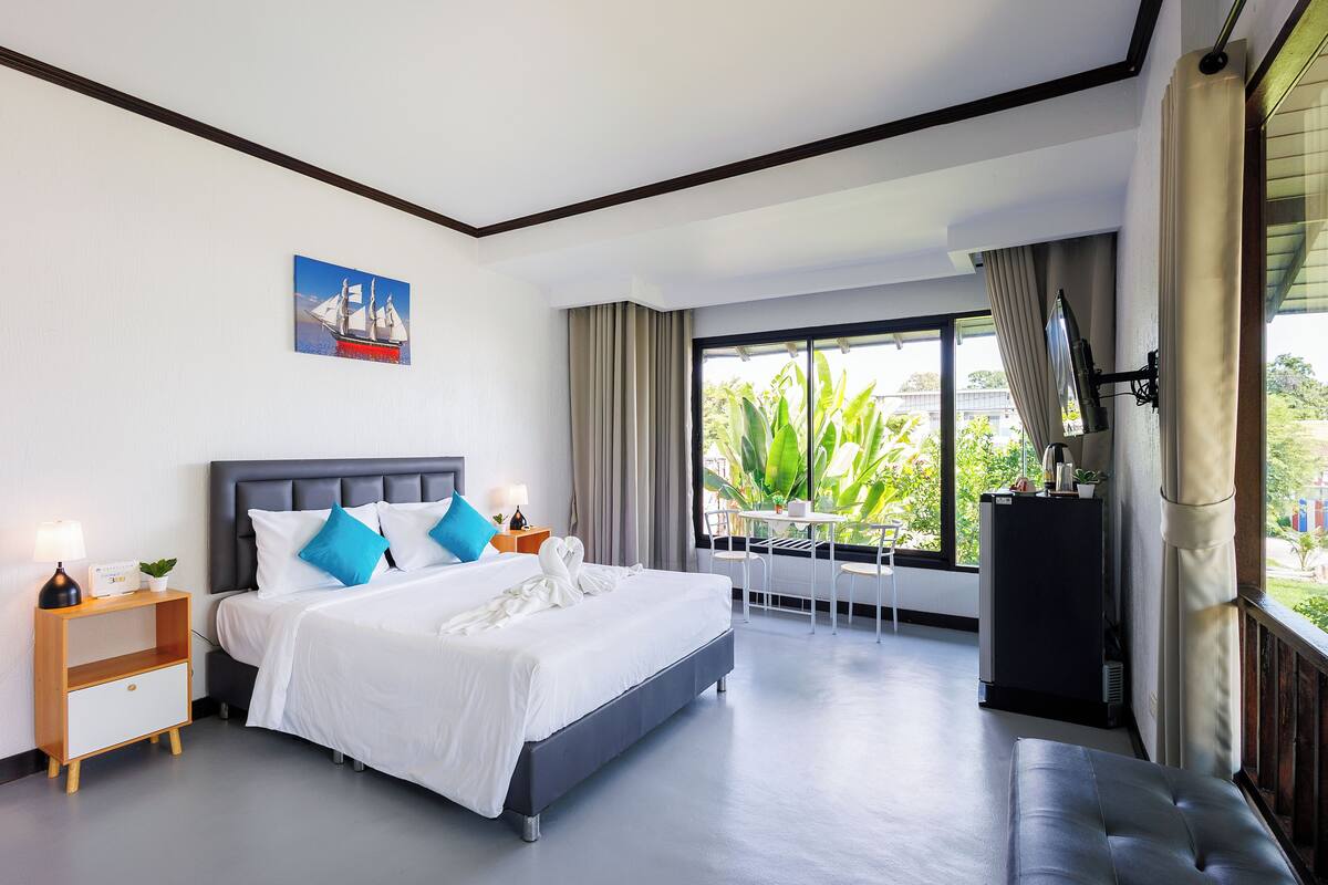 A modern hotel room with a large bed, a desk, and a view of the outdoors.