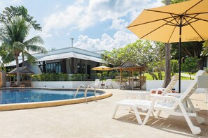 A swimming pool with lounge chairs and umbrellas, surrounded by palm trees and a modern building. - Peace Garden Resort Koh Samui (Koh Samui)