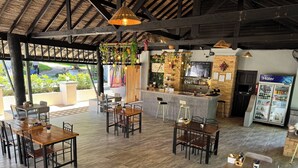 A restaurant with wooden tables and chairs, a bar area, and a refrigerator. - Peace Garden Resort Koh Samui (Koh Samui)