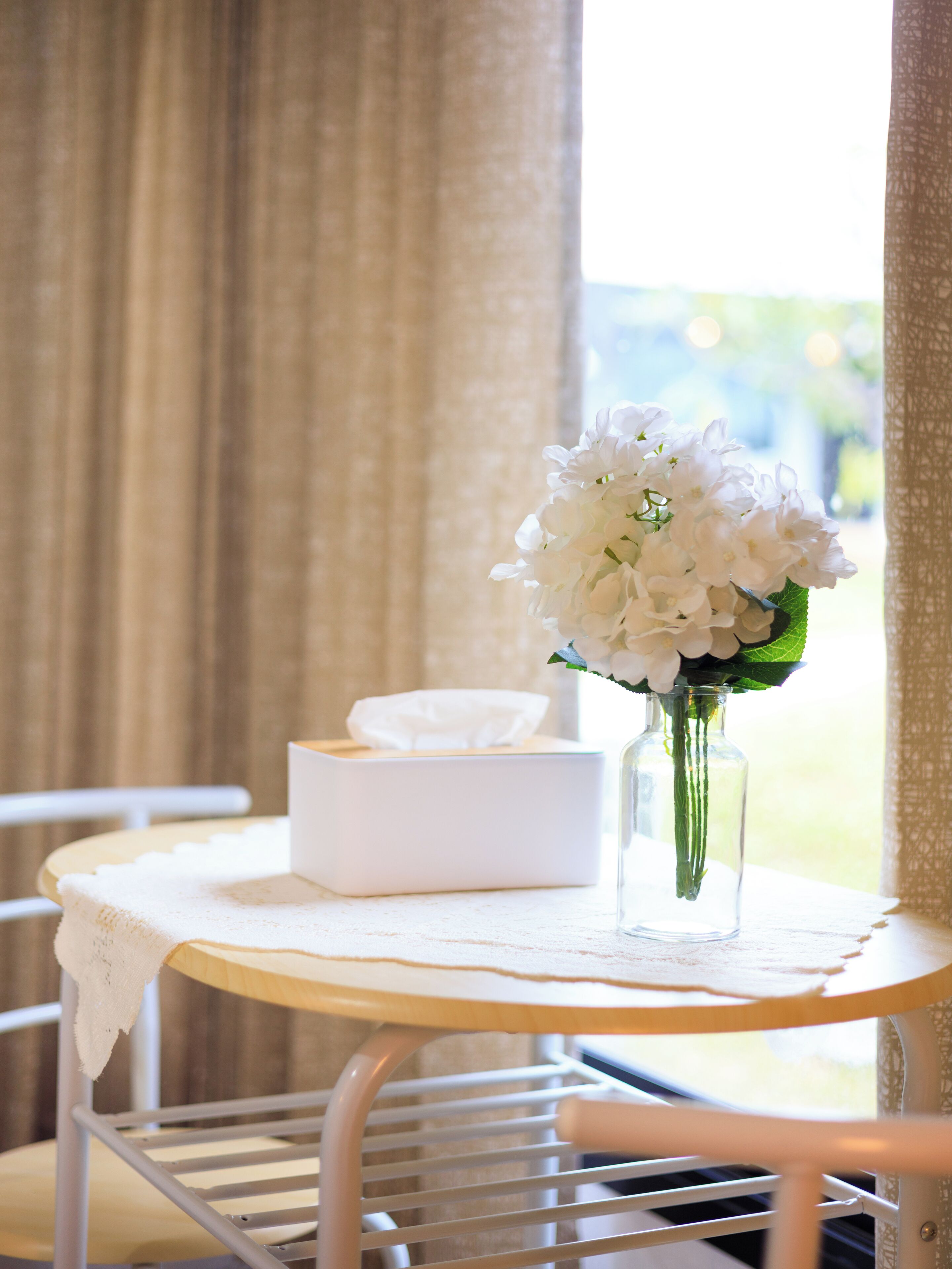 A table with a tissue box and a vase of white flowers.
