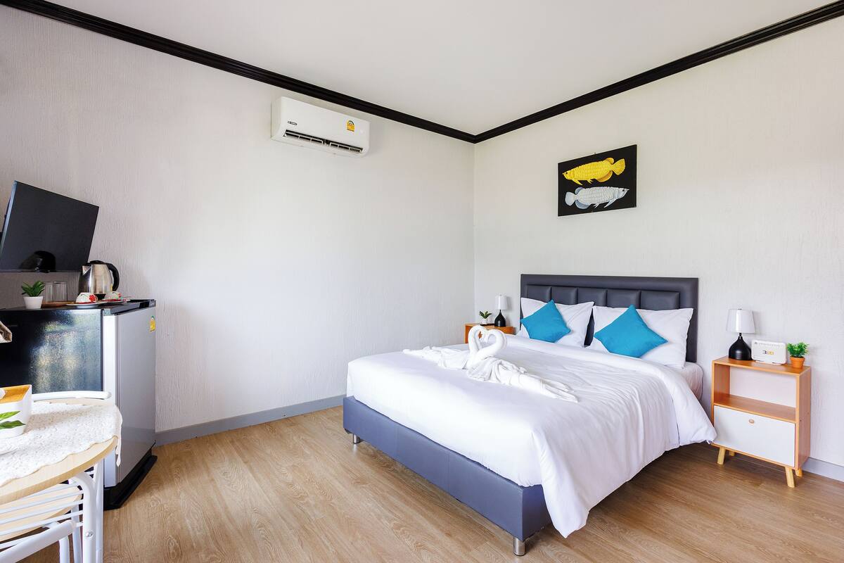 A neatly arranged hotel room with a bed, bedside table, and a small desk with a television and a kettle.