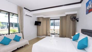 Habitación de hotel con cama, sofá, televisión y ventana con cortinas.