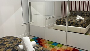 Un dormitorio con cama, alfombra colorida, armario y ventana con cortinas.