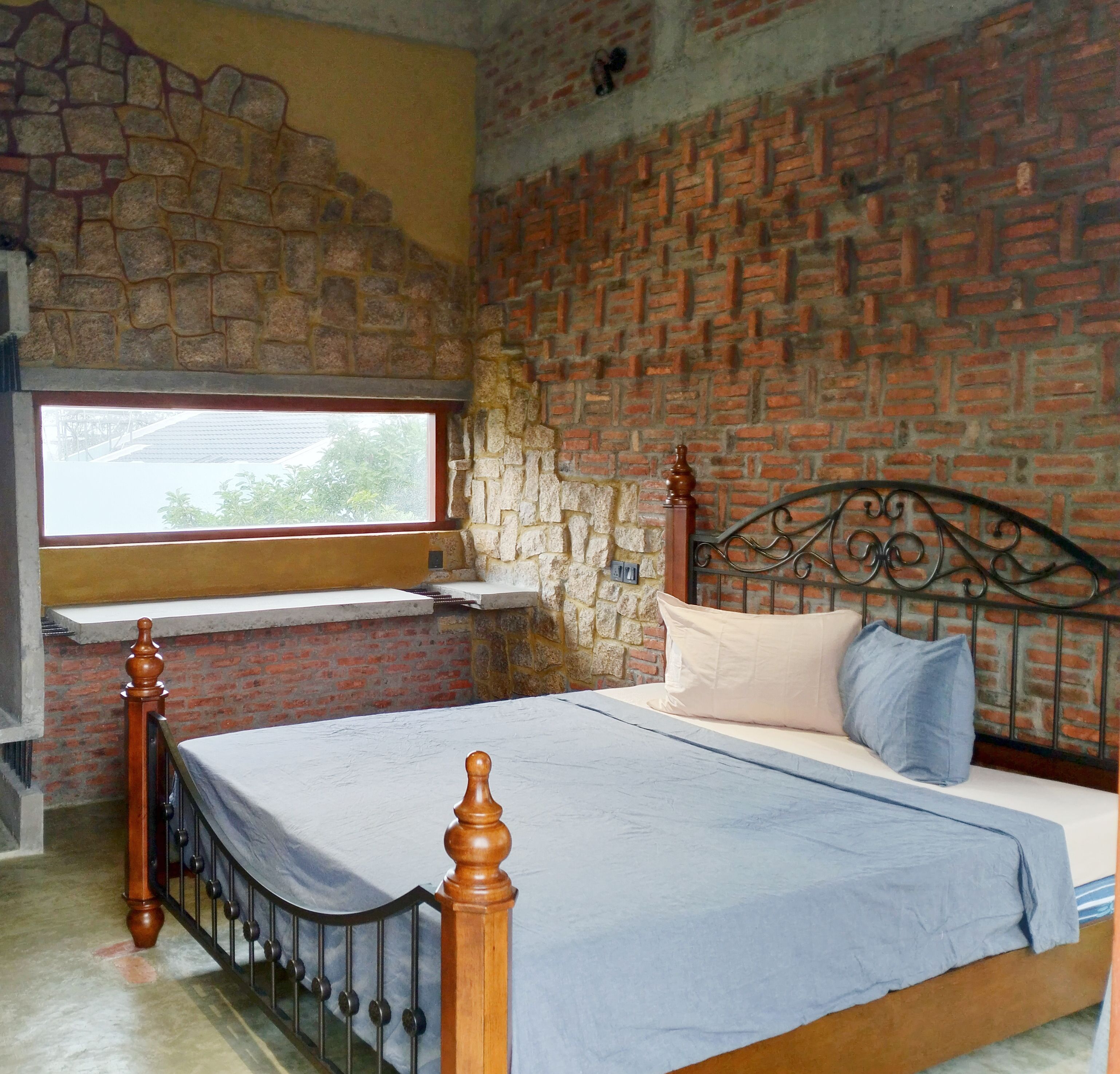 Un dormitorio con pared de ladrillo, ventana, cama con cabecera de madera y pared de piedra.